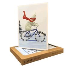 Load image into Gallery viewer, Brown box of holiday cards with greeting card displayed on top. Design features a polar bear wearing a red scarf, riding a blue bike through a snowy landscape.