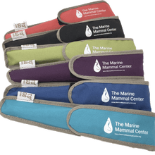 Load image into Gallery viewer, 6 utensil bags lay beside one another in light blue, dark blue, purple, green, black, and red. Each utensil bag is lined with grey borders, has a fabric "To Go" tag and shows The Marine Mammal Center name and logo with website address on the flap cover for the bag.