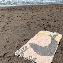 Load image into Gallery viewer, Peach and tan beach towel with harbor seal silhouette design, laid out on sand with ocean in background
