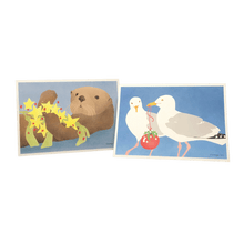 Load image into Gallery viewer, 2 holiday cards: sea otter holding yellow stars and kelp, and seagulls holding a red bauble.