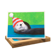 Load image into Gallery viewer, Holiday card with sea otter wearing striped hat, lying on its back against a blue and green background.