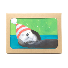 Load image into Gallery viewer, Box of holiday cards with sea otter wearing striped hat on cover.