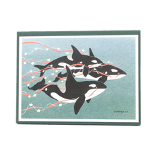 Load image into Gallery viewer, Holiday card box cover with 3 orcas (killer whales) swimming against green-blue background, trailing red streamers and yellow stars.
