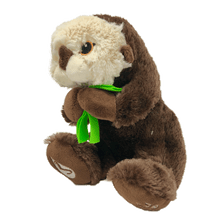 Load image into Gallery viewer, Plush brown and light tan sea otter with embroidered eyes holding bright green kelp. Embroidered feet show white The Marine Mammal Center name and logo in white thread.
