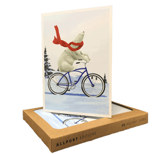 Brown box of holiday cards with greeting card displayed on top. Design features a polar bear wearing a red scarf, riding a blue bike through a snowy landscape. 