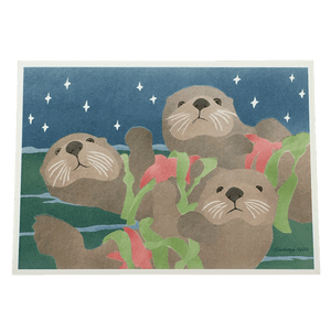 Holiday card featuring three sea otters floating on ocean surface, each holding a red sea star and fronds of green kelp. 