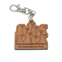 Load image into Gallery viewer, Brown wood rectangular keychain with the outlines of 10 sea lions and text &quot;The Marine Mammal Center&quot; laser-cut. Silver-colored metal clip attached to top. 
