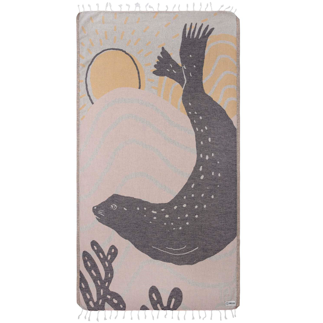Coral-colored beach towel with dark gray harbor seal silhouette and yellow sunrise design. White tassel fringe along top and bottom