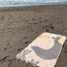 Load image into Gallery viewer, Peach and tan beach towel with harbor seal silhouette design, laid out on sand with ocean in background
