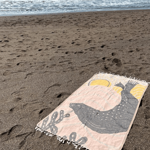 Peach and tan beach towel with harbor seal silhouette design, laid out on sand with ocean in background