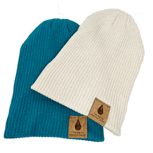 A turquoise and cream beanie lie on one another with the cuff unfolded.  The cork tags on the cuff depict The Marine Mammal Center Logo. 