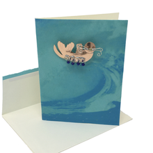 Load image into Gallery viewer, Blank greeting card with metal sea otter pin attached to light blue front cover, envelope below.
