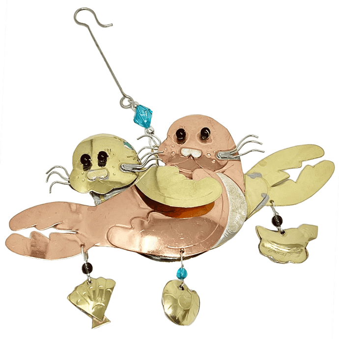 Silver and copper-colored metal ornament in shape of two seal pups, with blue and purple beads and metal shells hanging along bottom edge.