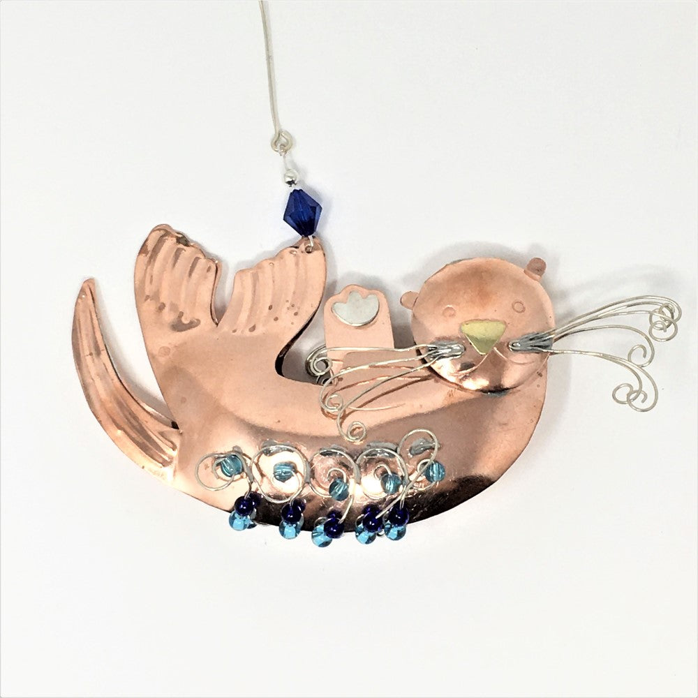 Copper and silver-colored metal ornament in shape of sea otter, with blue beads.