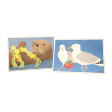 Load image into Gallery viewer, 2 holiday cards: sea otter holding yellow stars and kelp, and seagulls holding a red bauble.
