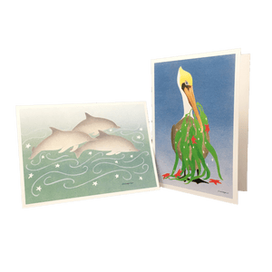 2 holiday cards: 3 dolphins swimming against green-blue background dotted with white stars, and pelican holding fronds of kelp and red stars in its beak.