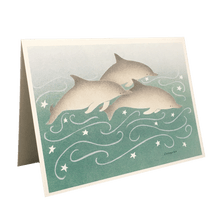 Load image into Gallery viewer, Holiday card with 3 dolphins swimming against green-blue background dotted with white stars.
