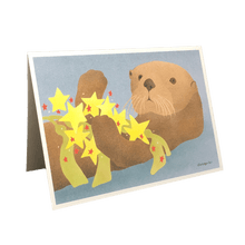 Load image into Gallery viewer, Holiday card with sea otter holding kelp and red and yellow stars.
