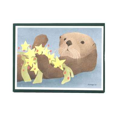 Holiday card box cover with sea otter holding yellow and red star ornaments and kelp.
