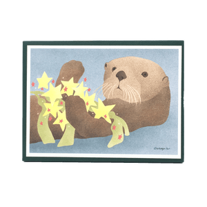Holiday card box cover with sea otter holding yellow and red star ornaments and kelp.