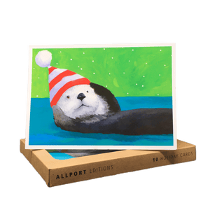 Holiday card with sea otter wearing striped hat, lying on its back against a blue and green background.