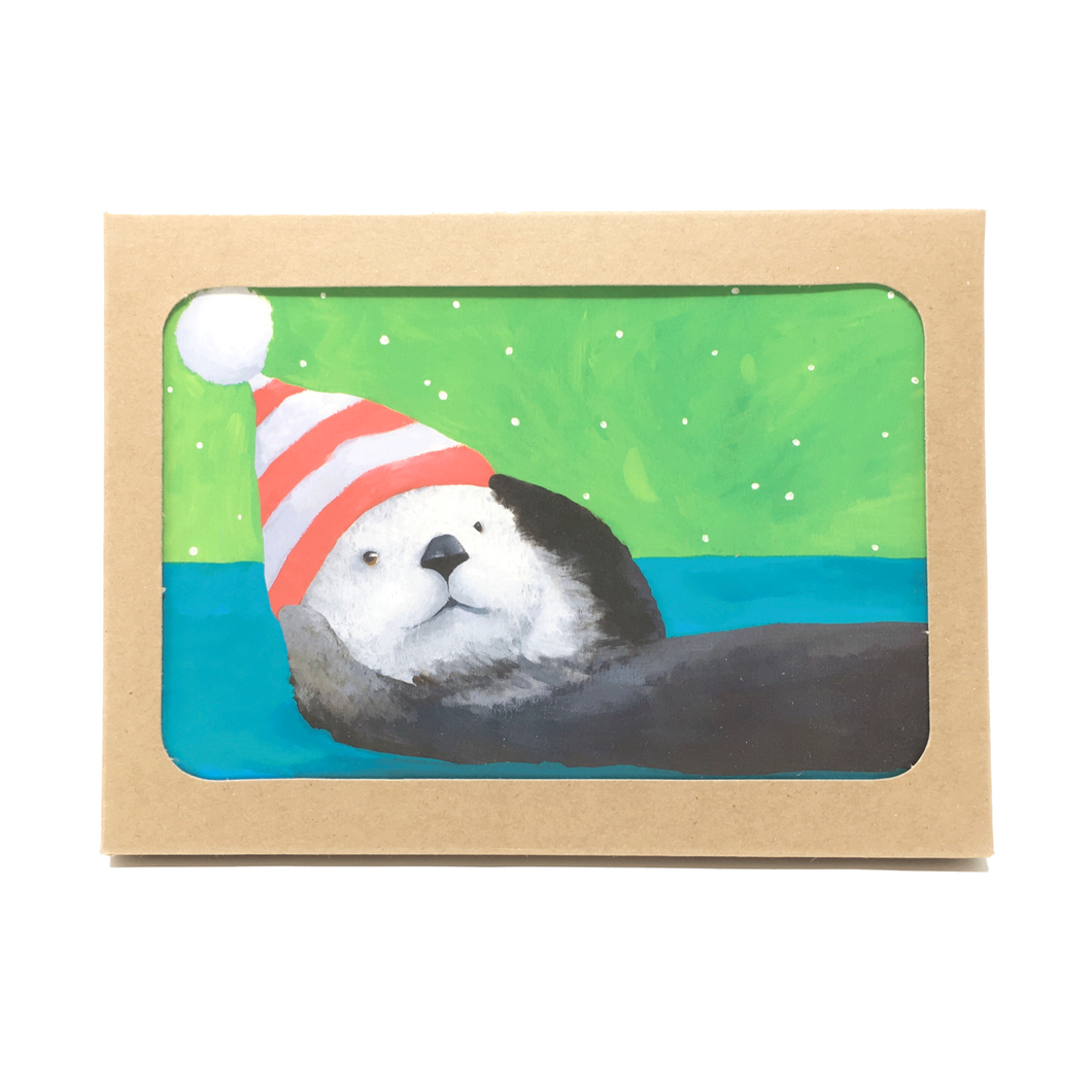 Box of holiday cards with sea otter wearing striped hat on cover.