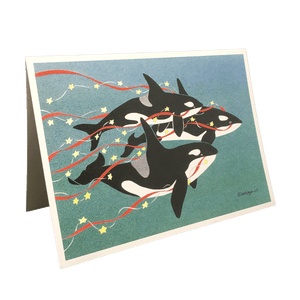 Holiday card with 3 orcas swimming against green-blue background, carrying red streamers and yellow stars.
