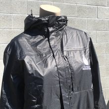 Load image into Gallery viewer, A headless mannequin&#39;s torso stands in front of a grey brick wall. The mannequin is wearing a black, shiny jacket fully zipped with a high collar and white The Marine Mammal Center chest logo on the left-hand side.
