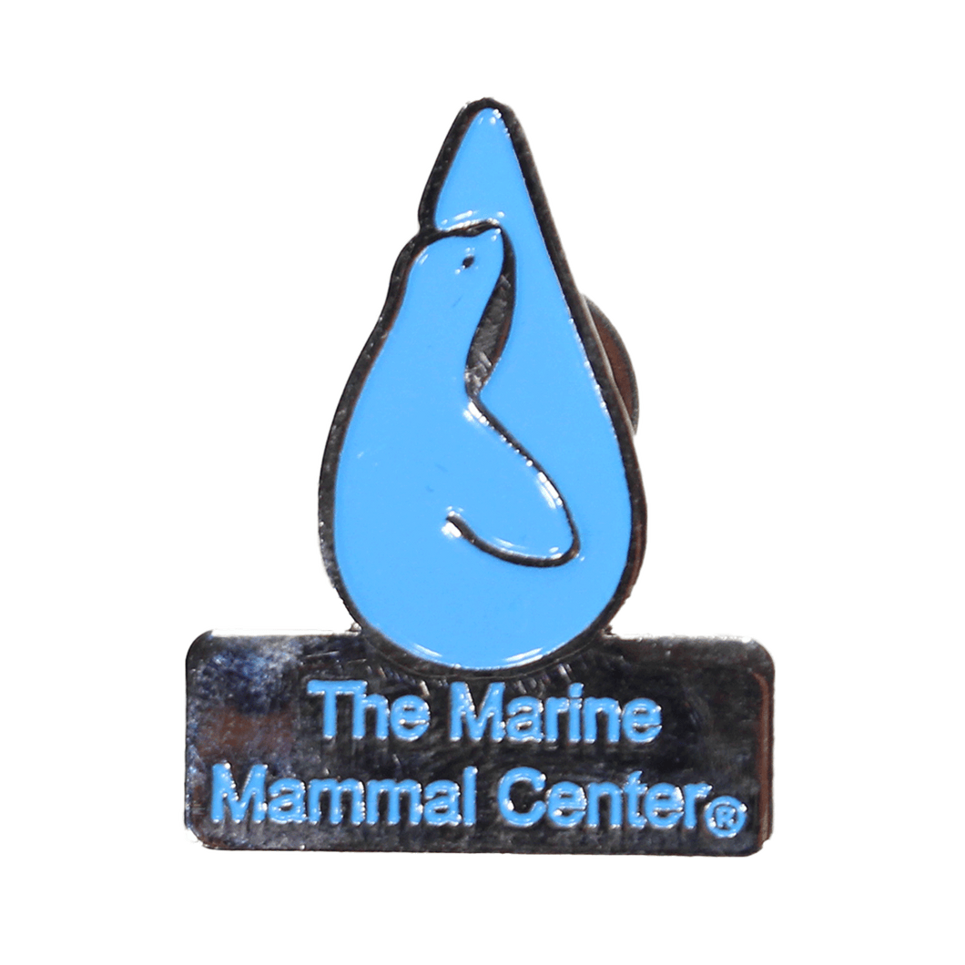 Light blue enamel pin with The Marine Mammal Center logo and name with trademark, silver lining backs the pin and outlines the logo and name.