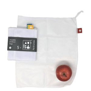 A mesh white reusable produce bag with a red tag lays flat on a surface, a 5-pack of white reusable mesh bags sits folded in black packaging with white lettering on top. A red apple sits on the laid out bag in the bottom right corner.