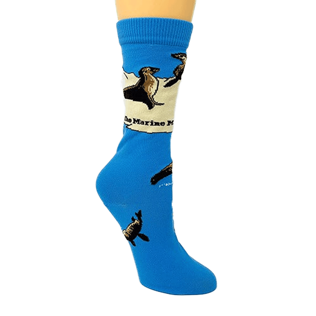 Light, vibrant blue sock on a mannequin foot. Sea lions swim in the blue color of the foot of the sock, and sea lion sit upright on flippers on the tan band around and above the ankle of the sock.