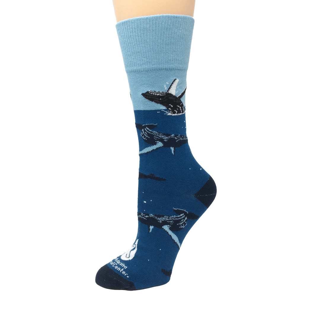 Blue socks with light blue cuff, dark blue heel and toe, and swimming and breaching humpback whale illustrations. The Marine Mammal Center's logo in white above toe.