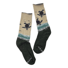 Load image into Gallery viewer, Pair of crew-length socks with design of baby sea turtles entering the ocean from the beach. Tan upper half and forest-green lower half.

