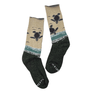 Pair of crew-length socks with design of baby sea turtles entering the ocean from the beach. Tan upper half and forest-green lower half.