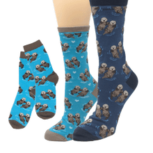 Load image into Gallery viewer, Socks in various shades of blue featuring pattern of sea otters holding hands
