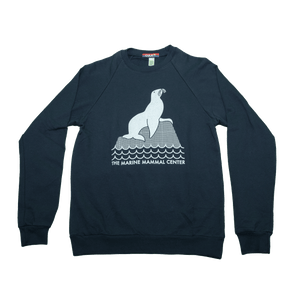 Navy blue sweatshirt with design in white of a sea lion perched on a rock above waves. Below the waves are the words THE MARINE MAMMAL CENTER in all caps.