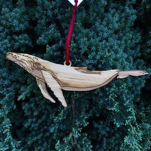 Wood humpback whale ornament against evergreen tree background.