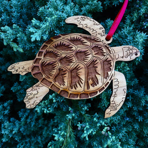 Wood sea turtle ornament against evergreen tree background.