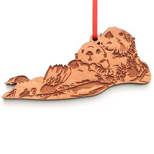 Laser-cut sea otter on their back with pup on their stomach, thin red ribbon strung through wooden hole at top of the ornament.